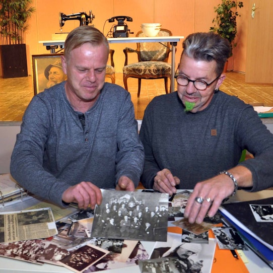 Zwei Männer, Andreas Bellgardt (links) und René Koder, sitzen an einem Tisch und betrachten historische Schwarz-Weiß-Fotos.