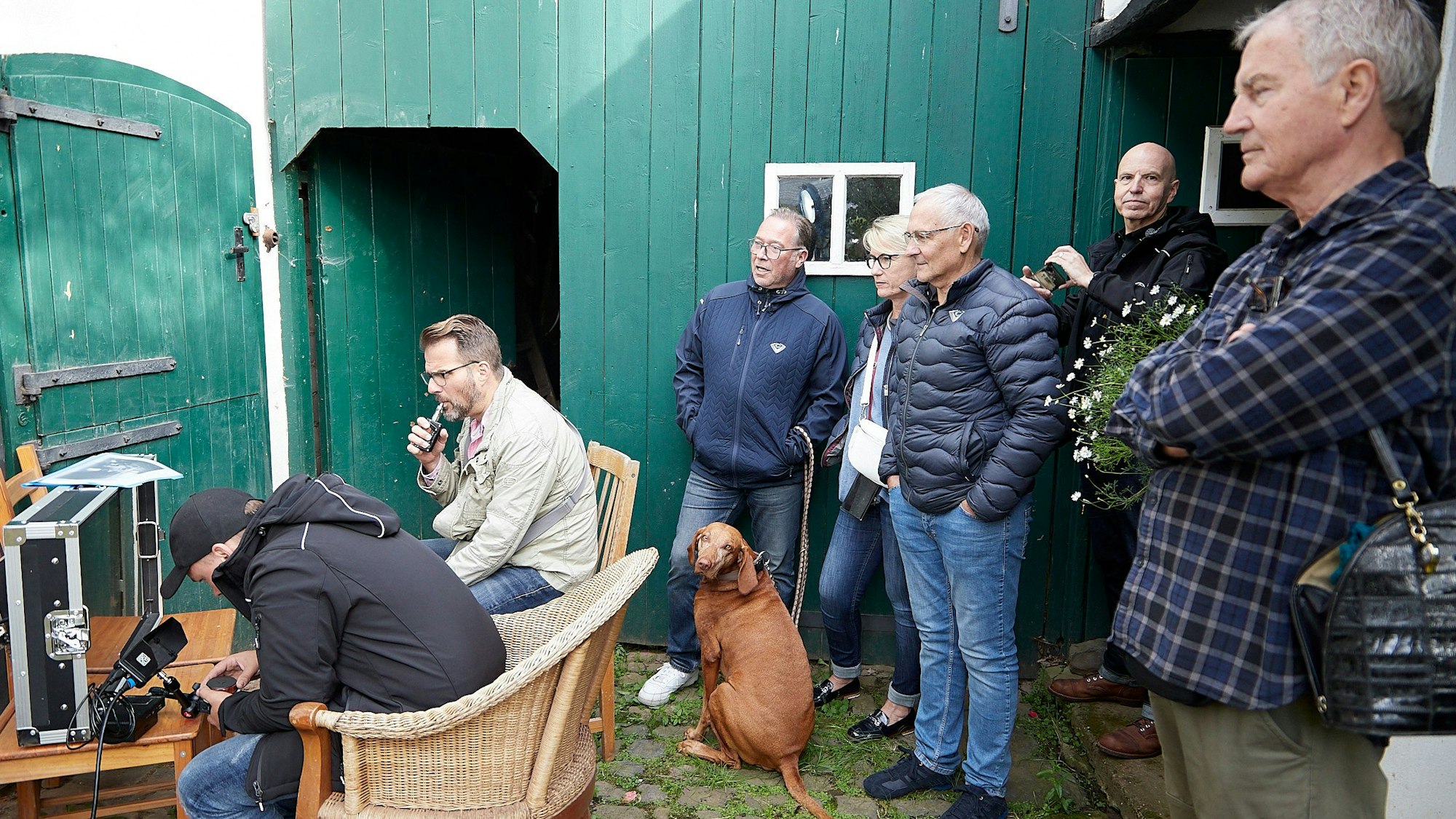 Ein Mann sitzt in einem Innenhof an einem Tisch vor einem Monitor, der in einem Transportkoffer untergebracht ist. Hinter ihm stehen weitere Menschen und schauen auf den Monitor.