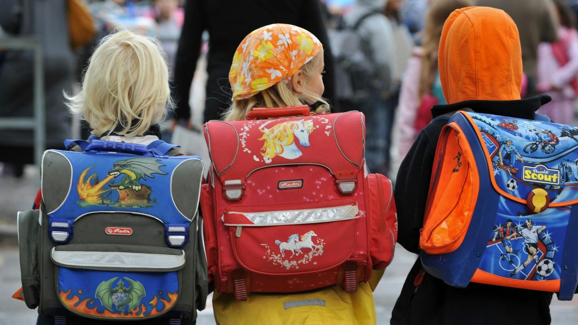 Drei Kinder von hinten mit Ranzen.