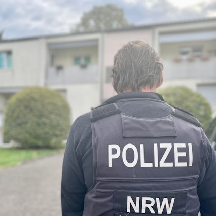 Das Bild zeigt einen Polizisten vor einem Haus.