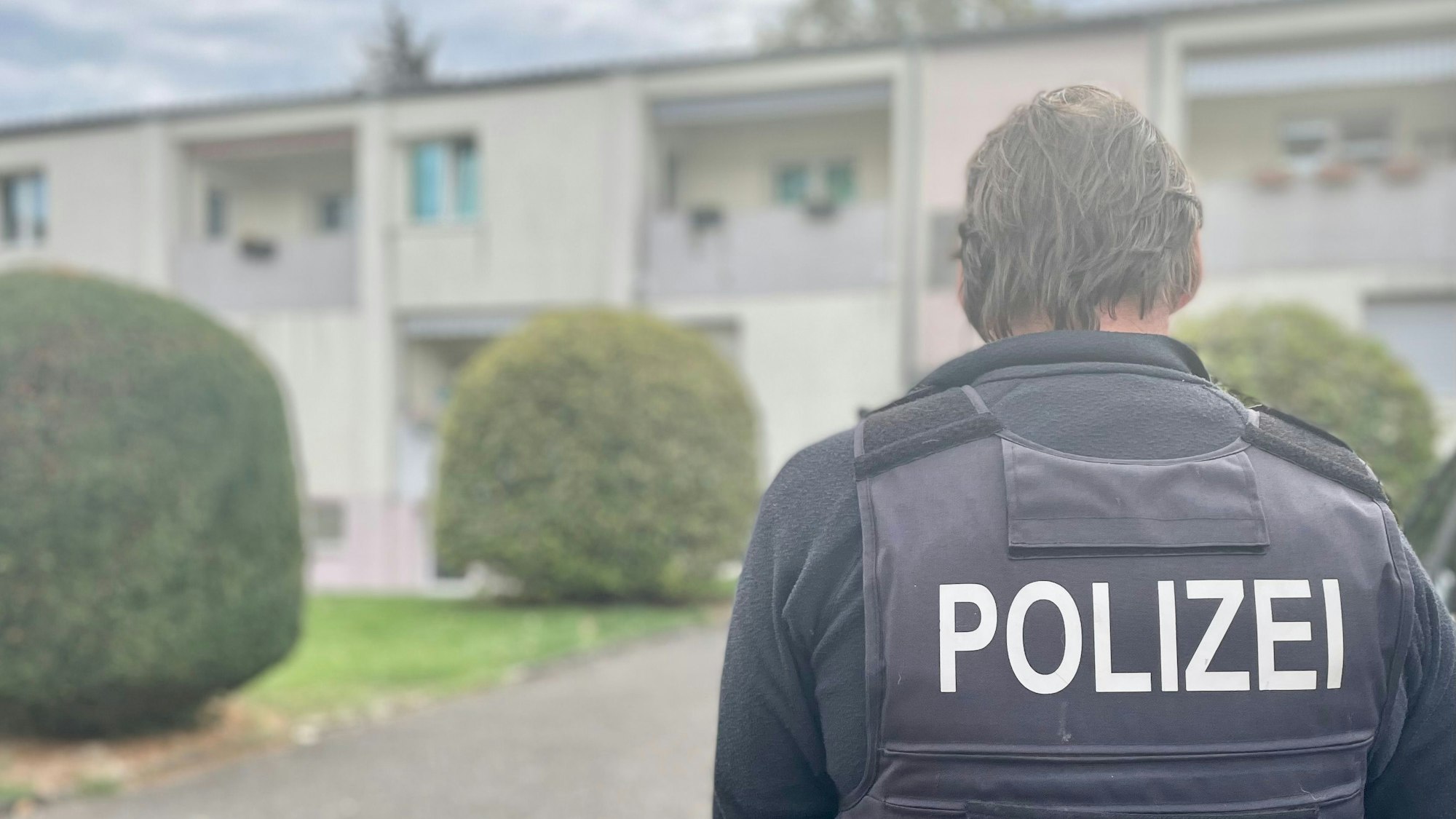 Das Bild zeigt einen Polizisten vor einem Haus.