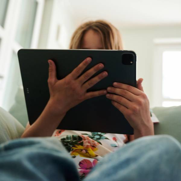 Ein Mädchen sitzt auf der Couch und guckt in das Tablet ihrer Eltern.