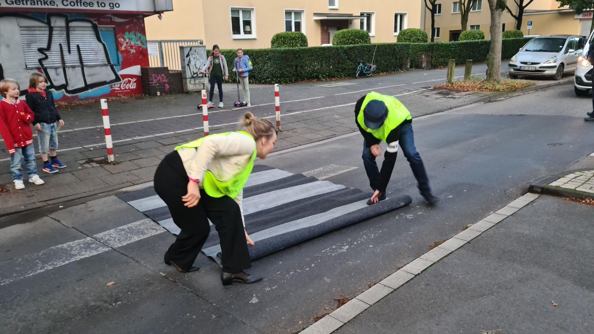 Helfer rollen einen Zebrastreifen-Teppich auf der Straße aus.