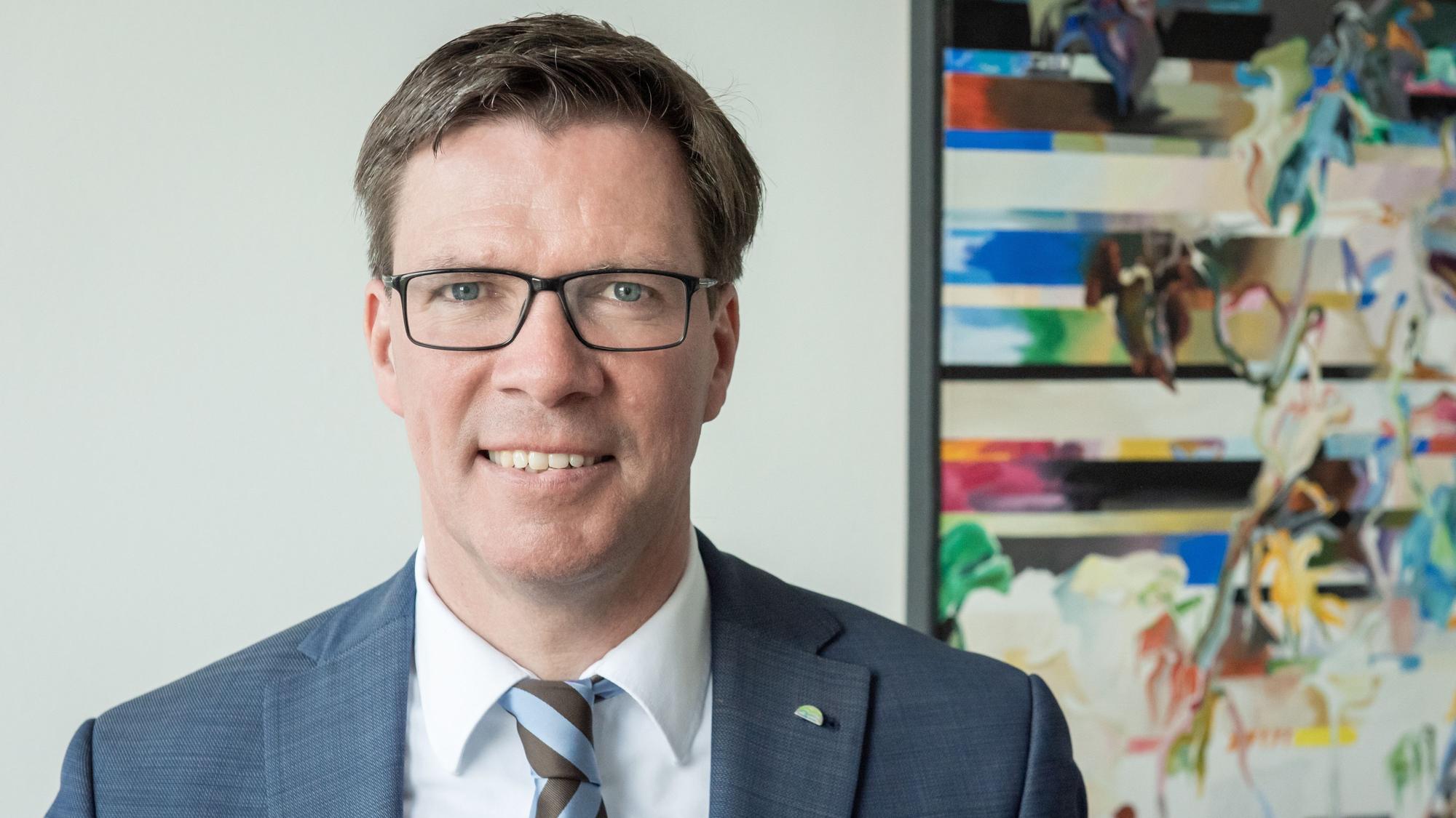 Landrat Stephan Santelmann steht vor einem bunten Bild im Kreishaus.