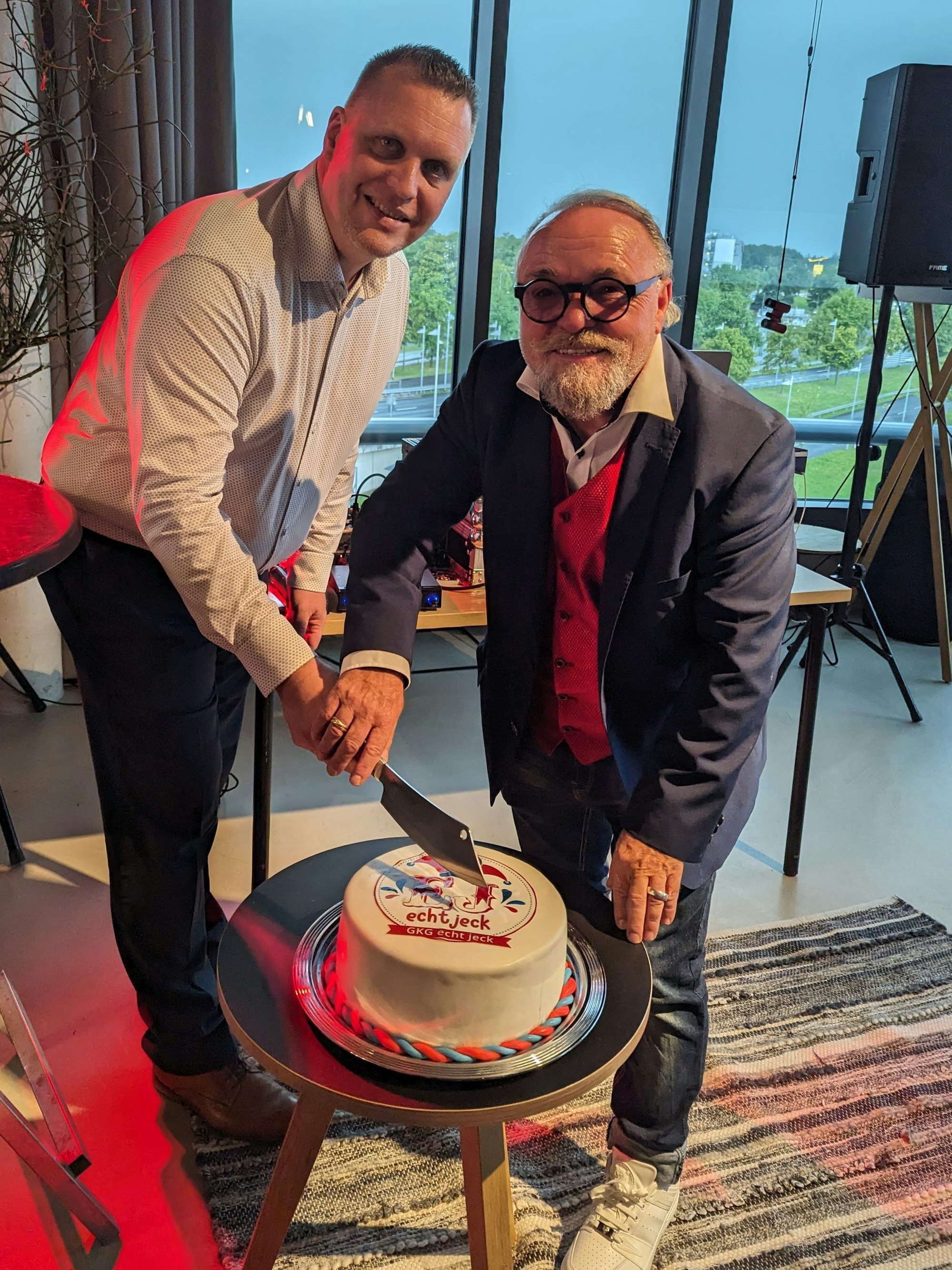 Zwei Männer schneiden gemeinsam eine Torte an, die mit dem Logo der GKG Echt Jeck verziert ist.