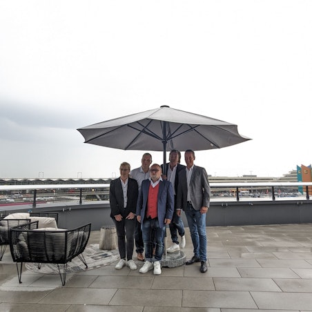 Gruppenbild auf einer Terrasse, im Hintergrund der Kölner Flughafen