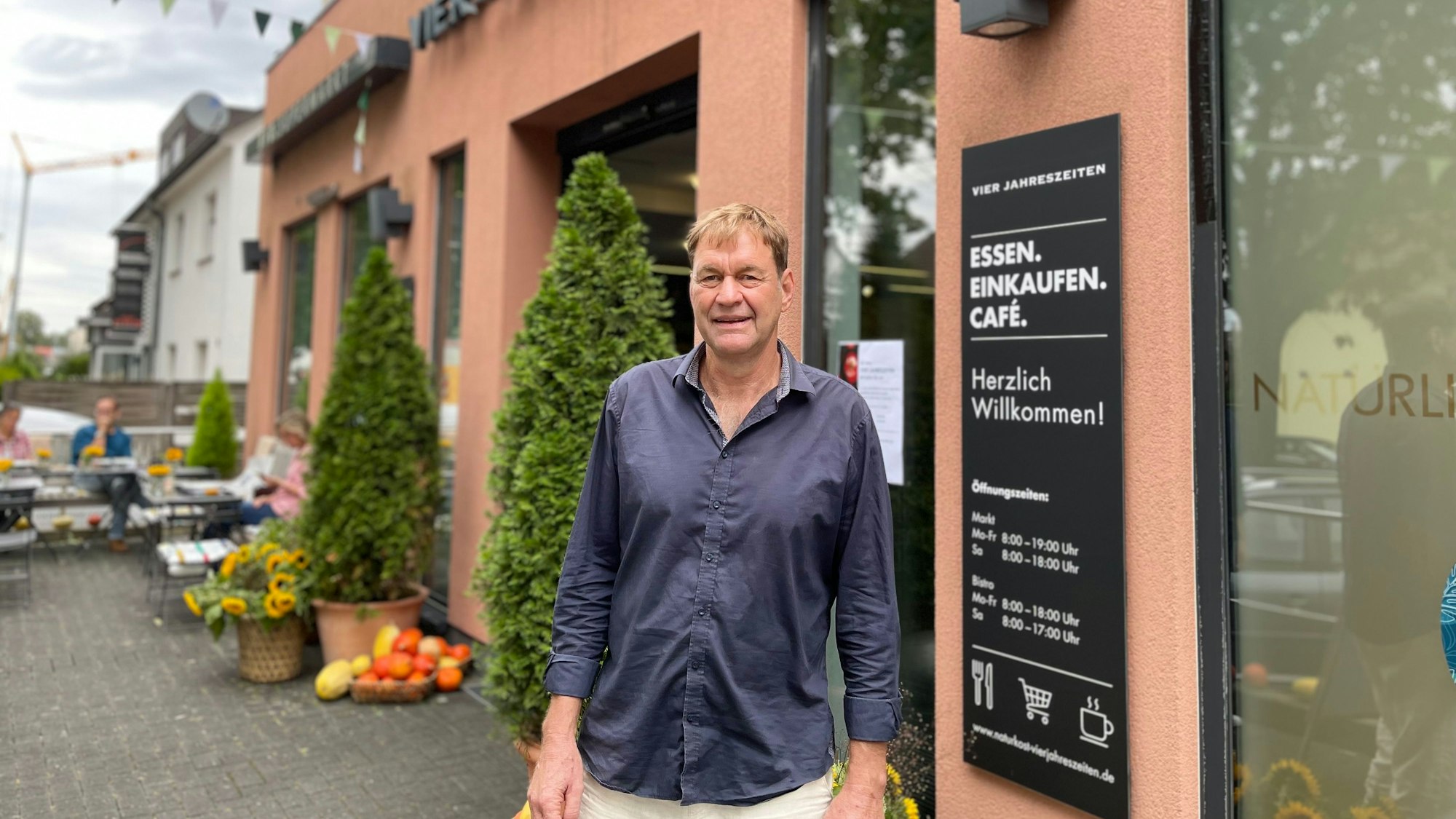 Ein Mann steht vor einer roten Hausfassade an einem schwarzen Schild mit der Beschriftung „Vier Jahreszeiten“.