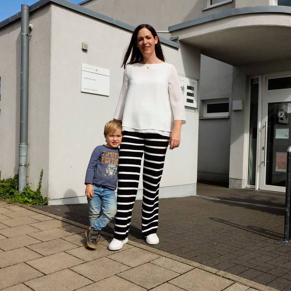 Eine Mutter steht mit ihrem dreijährigen Sohn vor dem Eingang einer Kita.