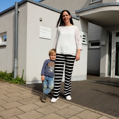 Eine Mutter steht mit ihrem dreijährigen Sohn vor dem Eingang einer Kita.