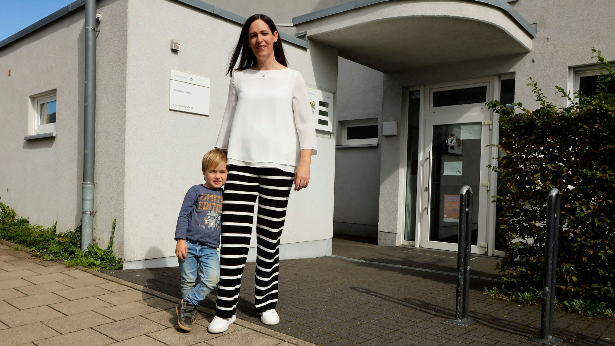 Eine Mutter steht mit ihrem dreijährigen Sohn vor dem Eingang einer Kita.