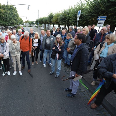 Eine Gruppe von Menschen steht auf der Rheinallee und der Stadtbahntrasse in der Altstadt von Königswinter.