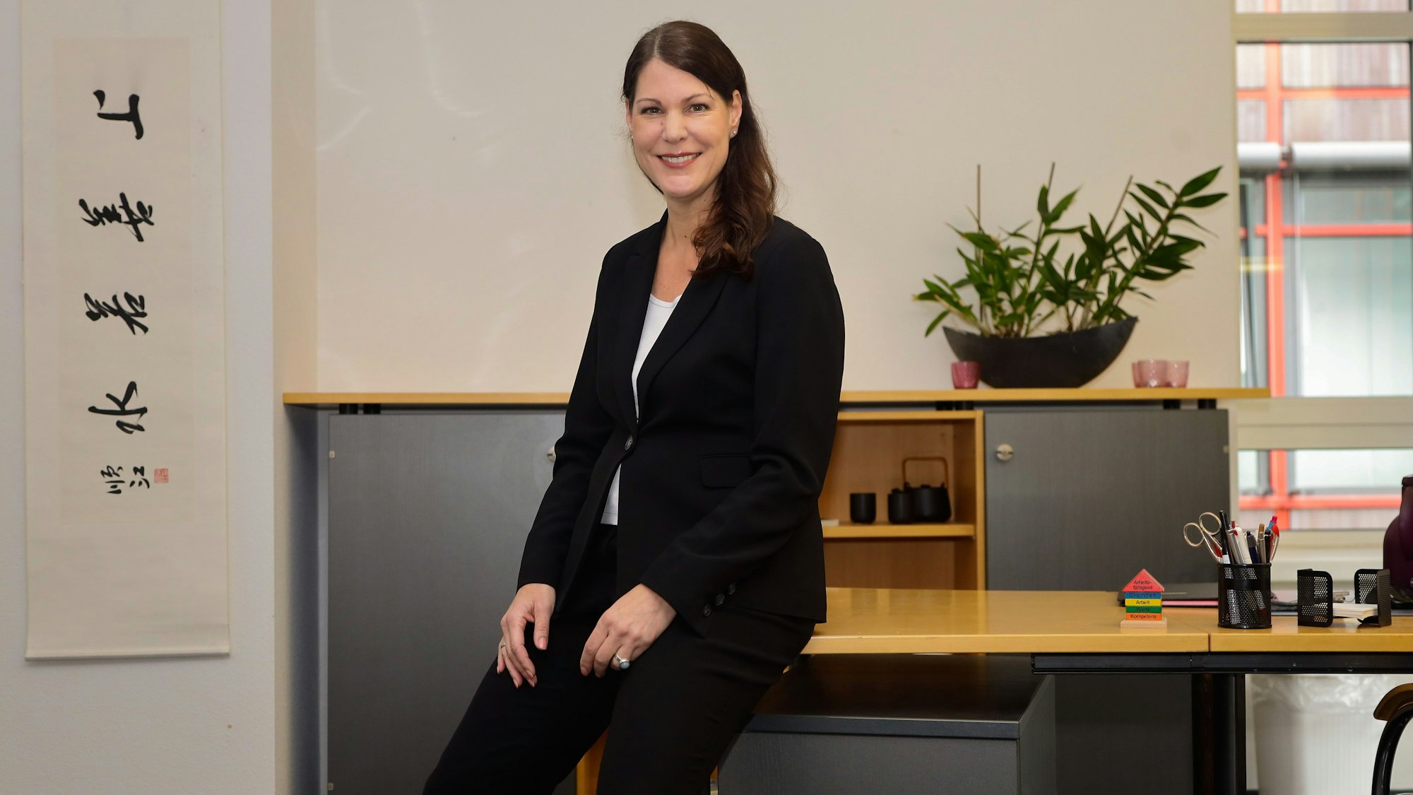 Athene Hammerich sitzt auf der Tischkante eines Schreibtischs in ihrem Büro.