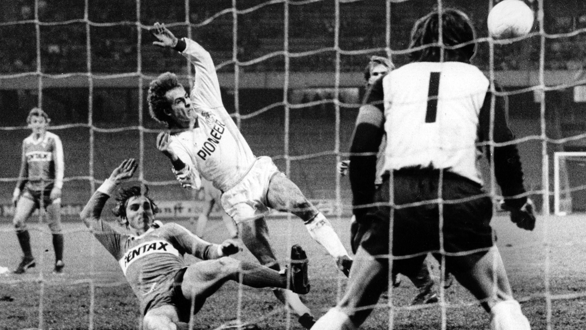 Auf der Schwarz-Weiß-Fotografie versucht sich der Spieler des 1. FC Köln Pierre Littbarski gegen seinen Bremer Gegenspieler im Strafraum durchzusetzen. Der Torhüter der Bremer beobachtet die Szene angespannt.