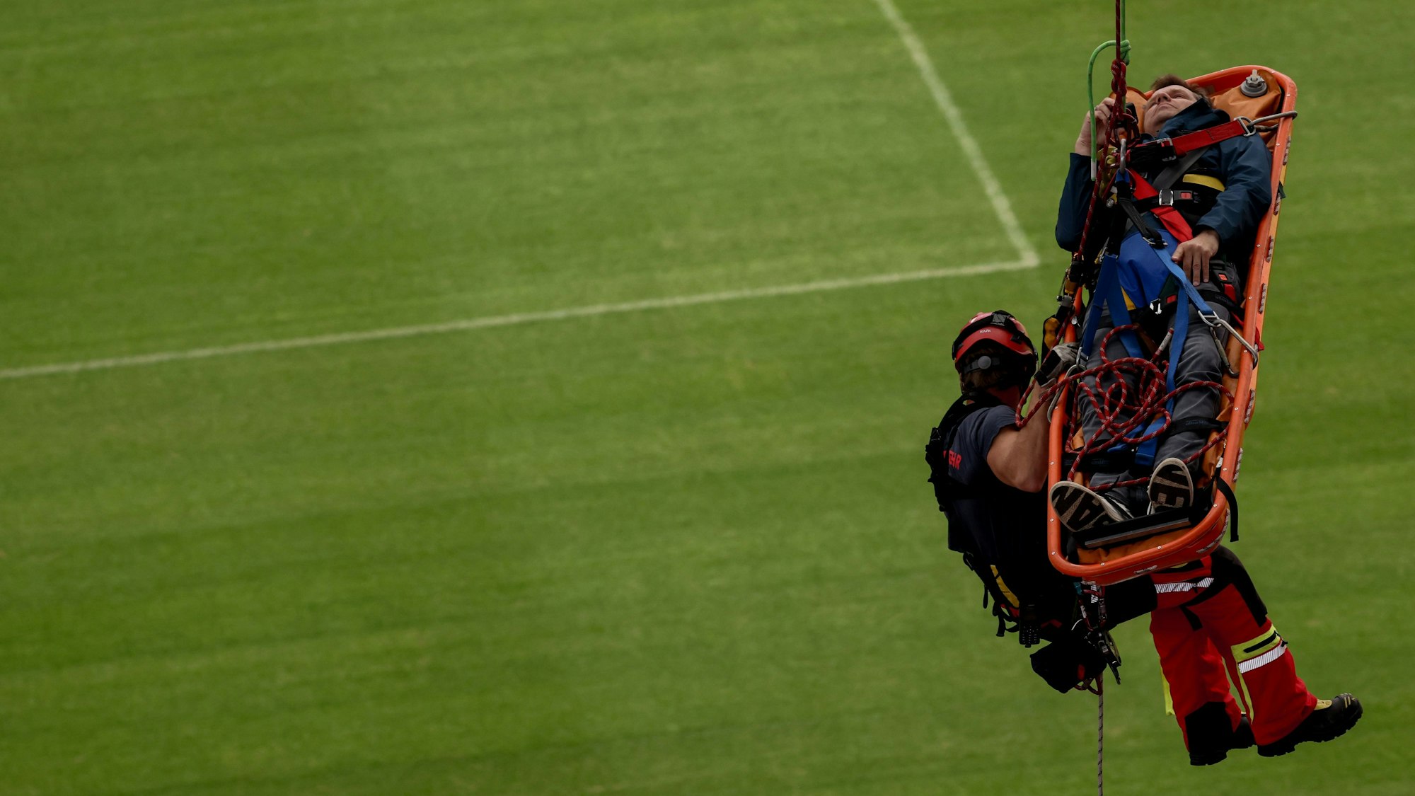 Ein Höhenretter der Feuerwehr und der Rettungskorb hängen über dem Stadionrasen in der Luft.