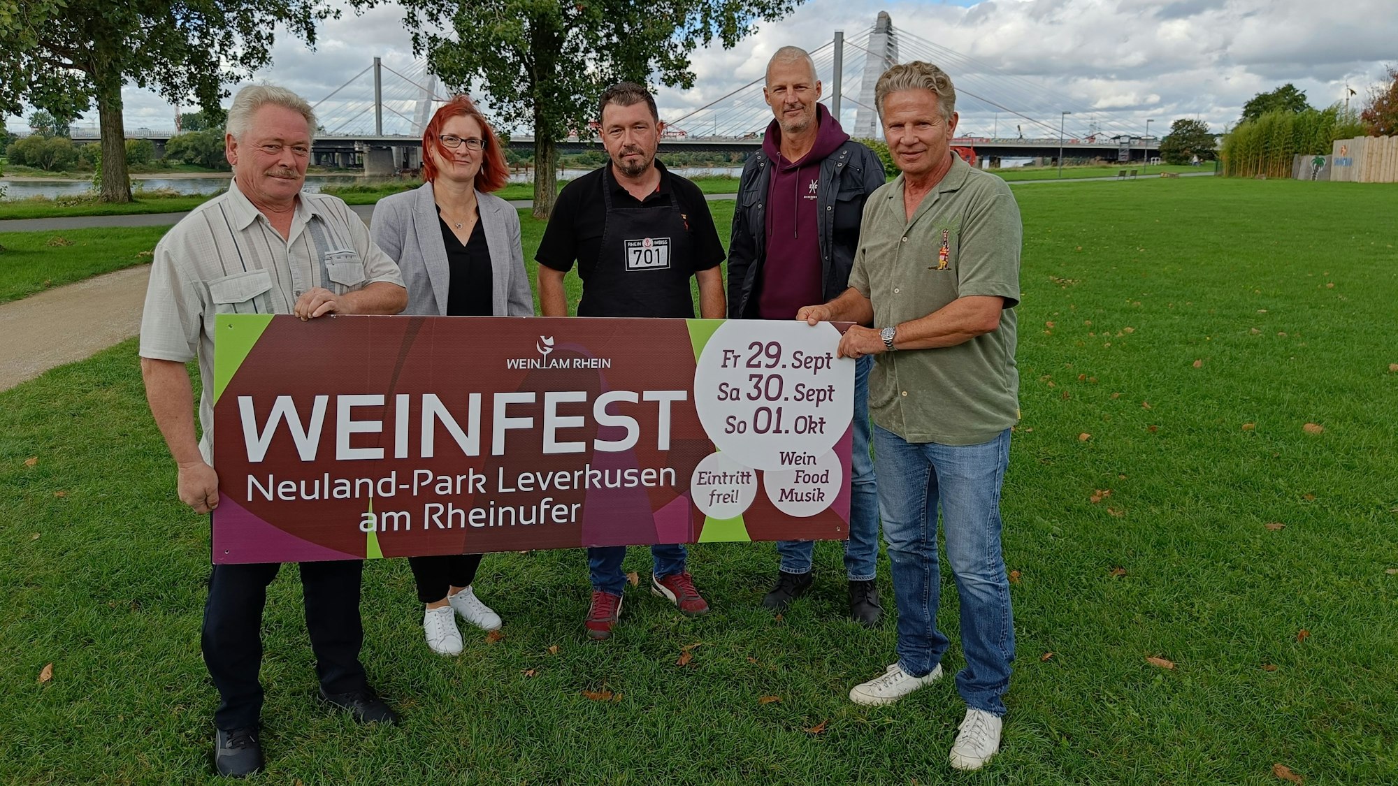 Eine Dame und vier Herren mit einem Werbebanner des Weinfests auf einer Wiese.