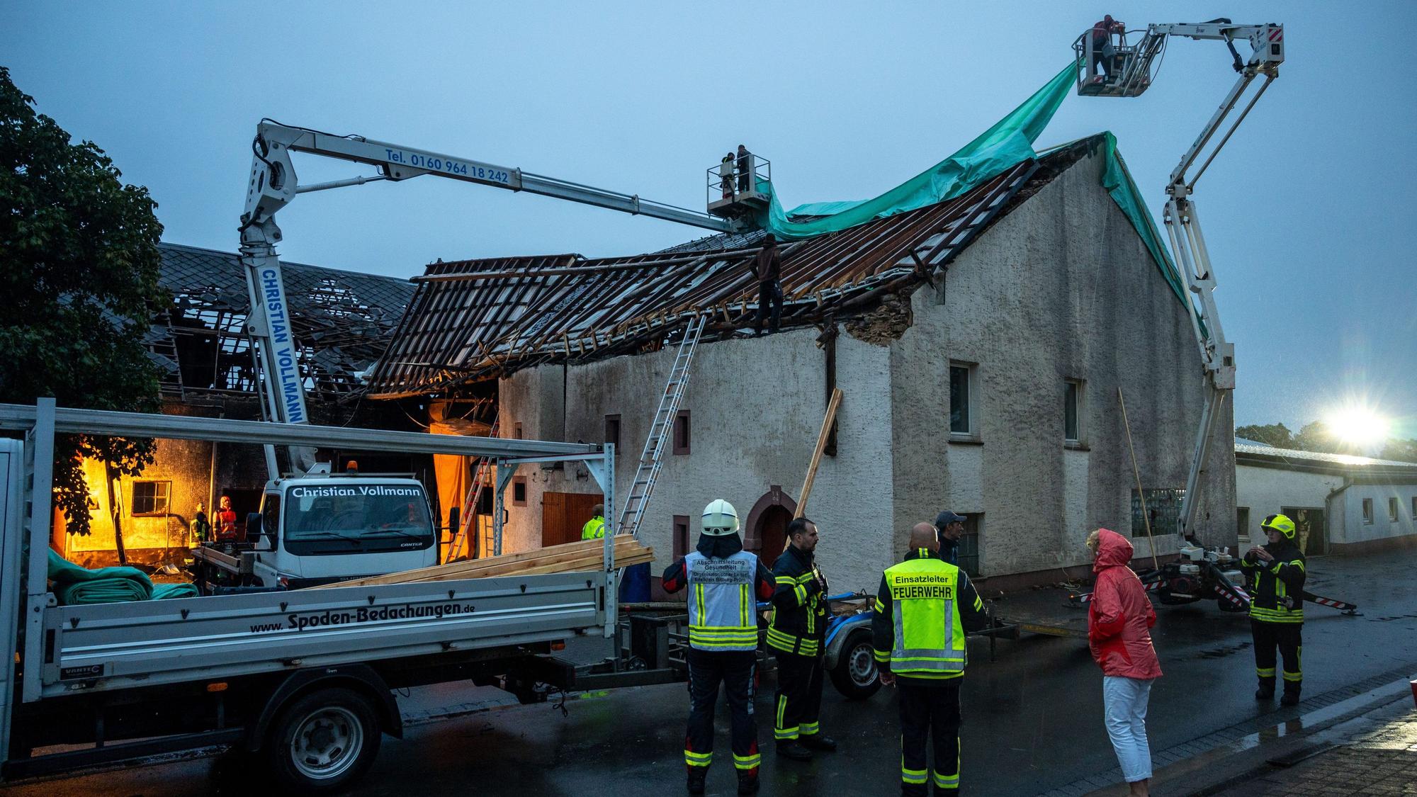 Feuerwehr und Einsatzkräfte kämpfen mit Schäden an einem abgedeckten Häuserdach im rheinland-pfälzischen Nusbaum, die durch einen Tornado verursacht wurden.