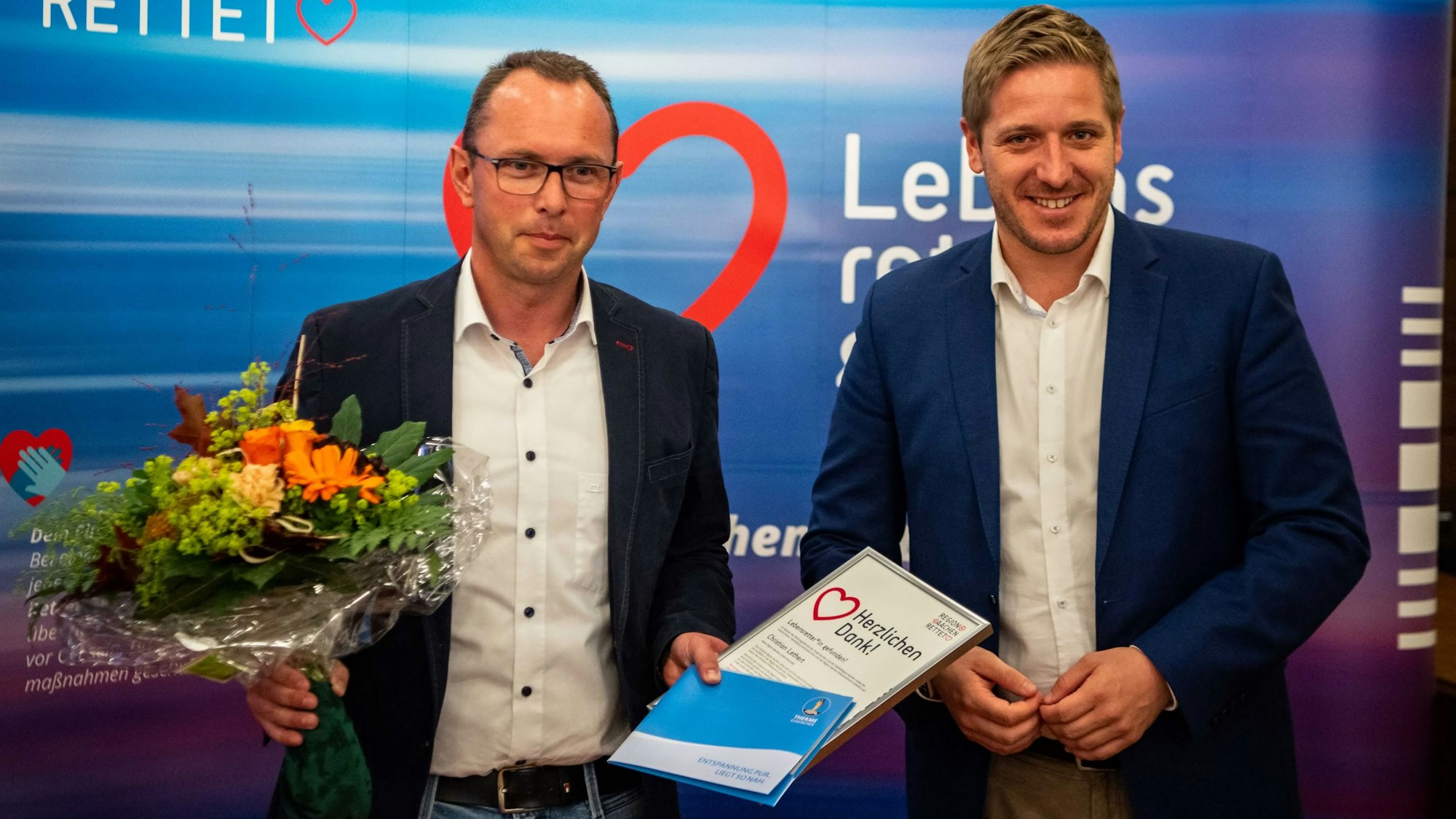 Das Bild zeigt Lebensretter Christian Lethert und Landrat Markus Ramers. Lethert hält einen Strauß Blumen und eine Urkunde in den Händen.