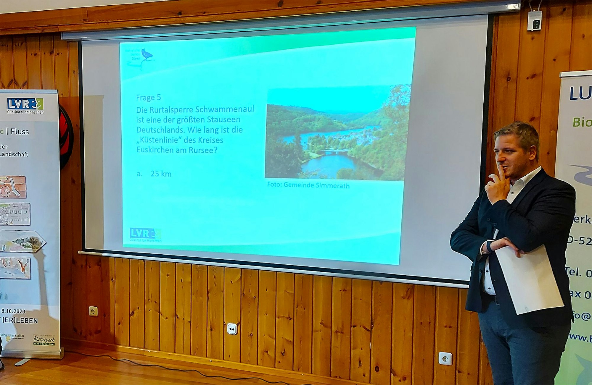 Landrat Markus Ramers steht vor einer Leinwand, auf der eine Quizfrage abgebildet ist.