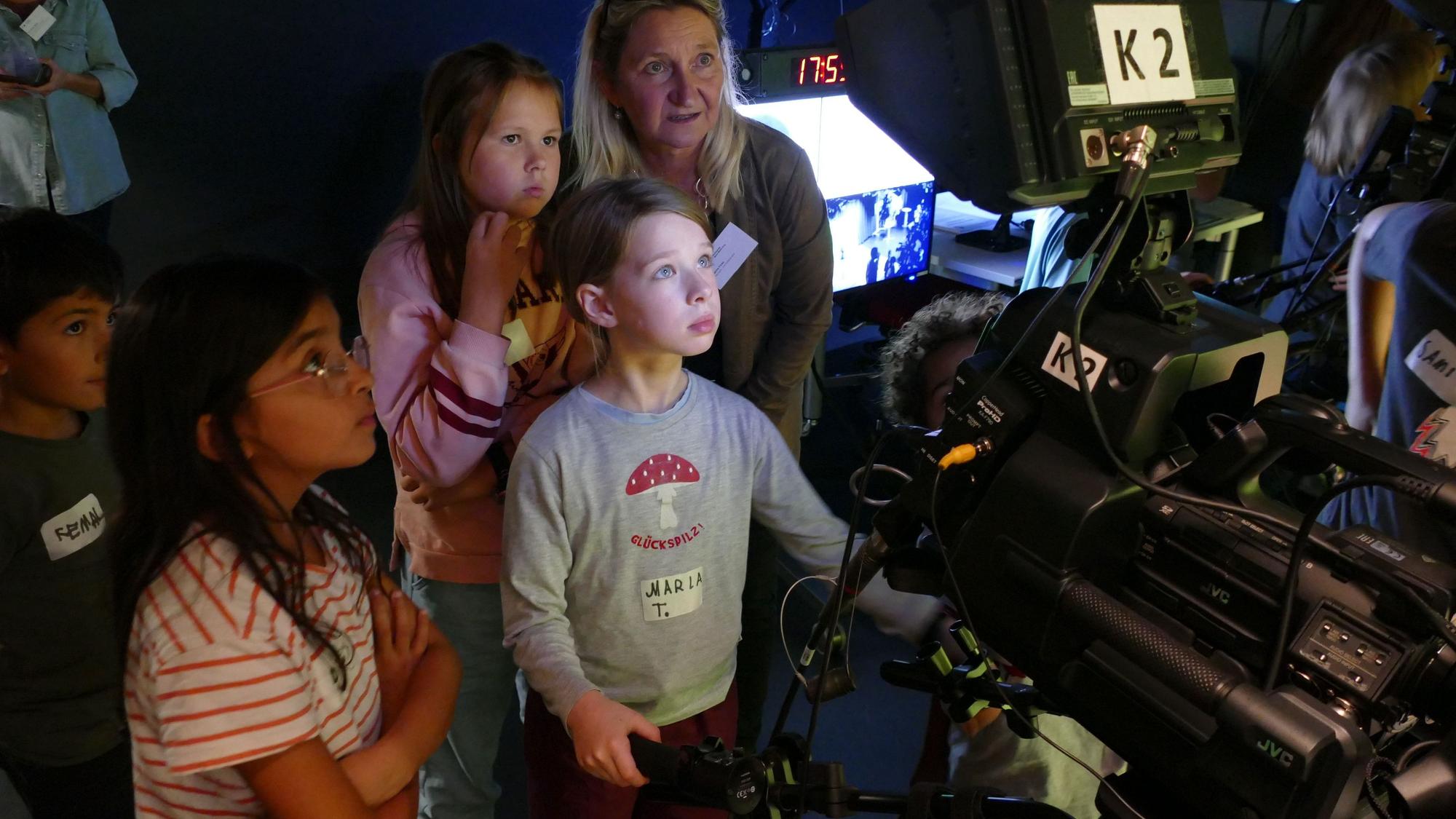 Drei Kinder und eine Erwachsene stehen hinter einer großen Filmkamera.