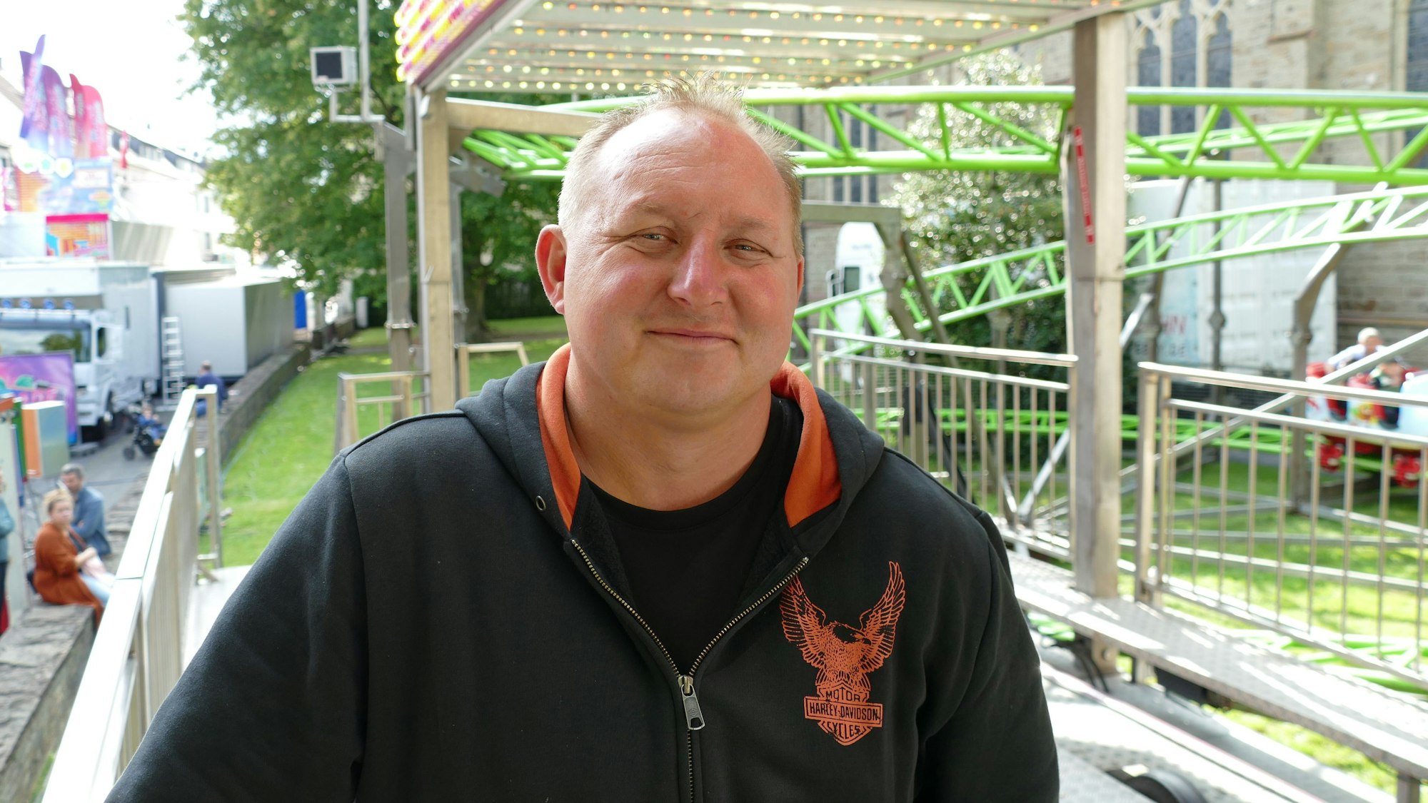 Ein Mann mit einem schwarzen Pullover steht vor der Gerüst eines Fahrgeschäfts.