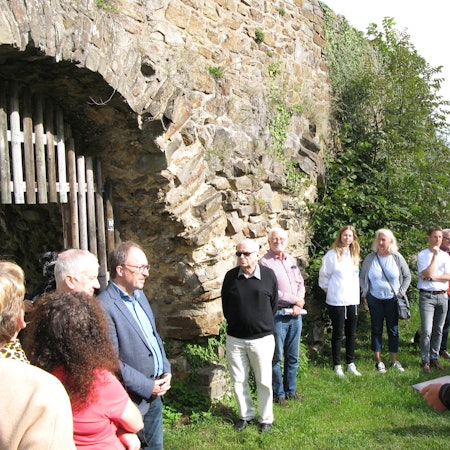 Eine Gruppe von Menschen steht mit dem Bürgermeister an der mittelalterlichen Stadtmauer von Stadt Blankenberg.