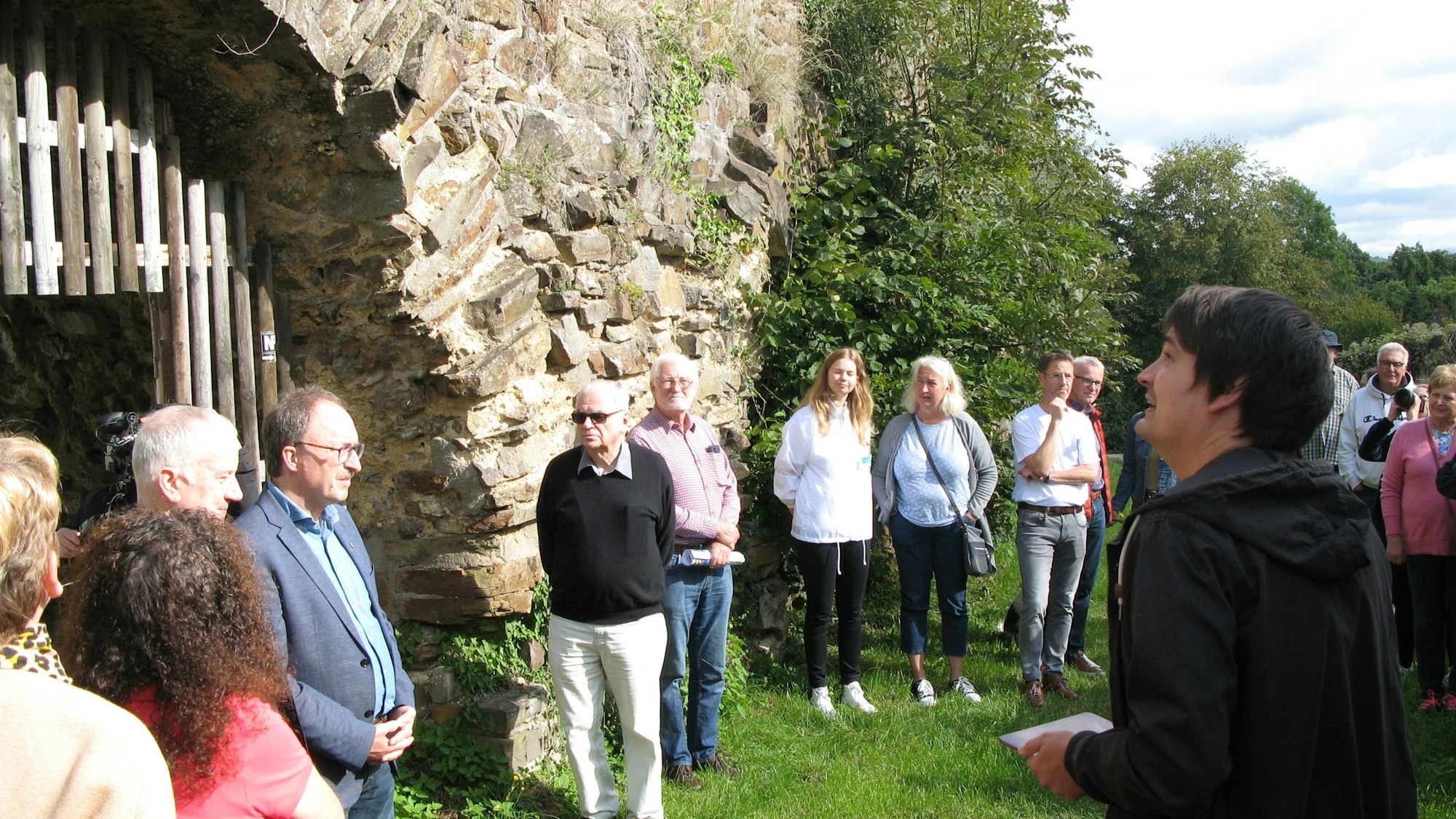 Eine Gruppe von Menschen steht mit dem Bürgermeister an der mittelalterlichen Stadtmauer von Stadt Blankenberg.