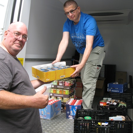 Ein Mann reicht einem anderen Mann, der in einem Transporter steht einen Karton mit gespendeten Lebensmitteln an.