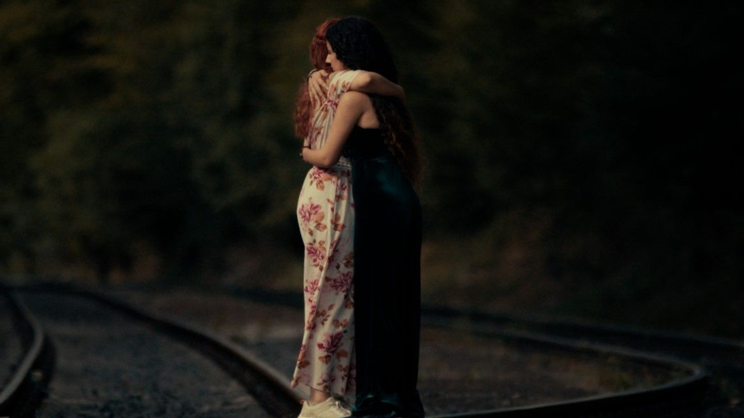 Zwei junge Frauen stehen auf Bahngleisen und umarmen sich.