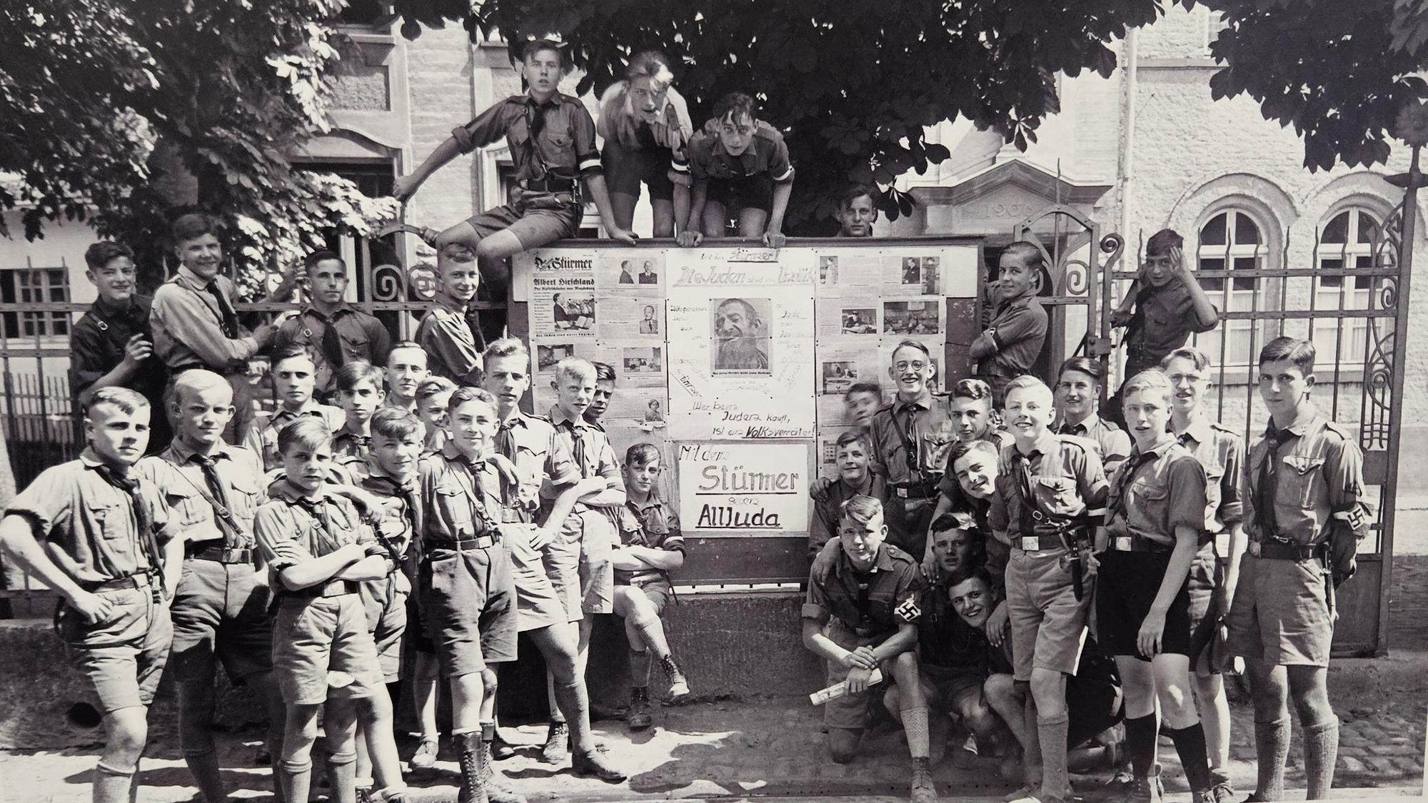 Jungen in HJ-Uniformen stehen vor einem großen Schaukasten.