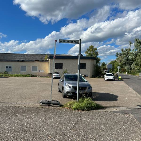 Ein fast leerer Parkplatz vor einem einstöckigen Gebäude ist zu sehen.