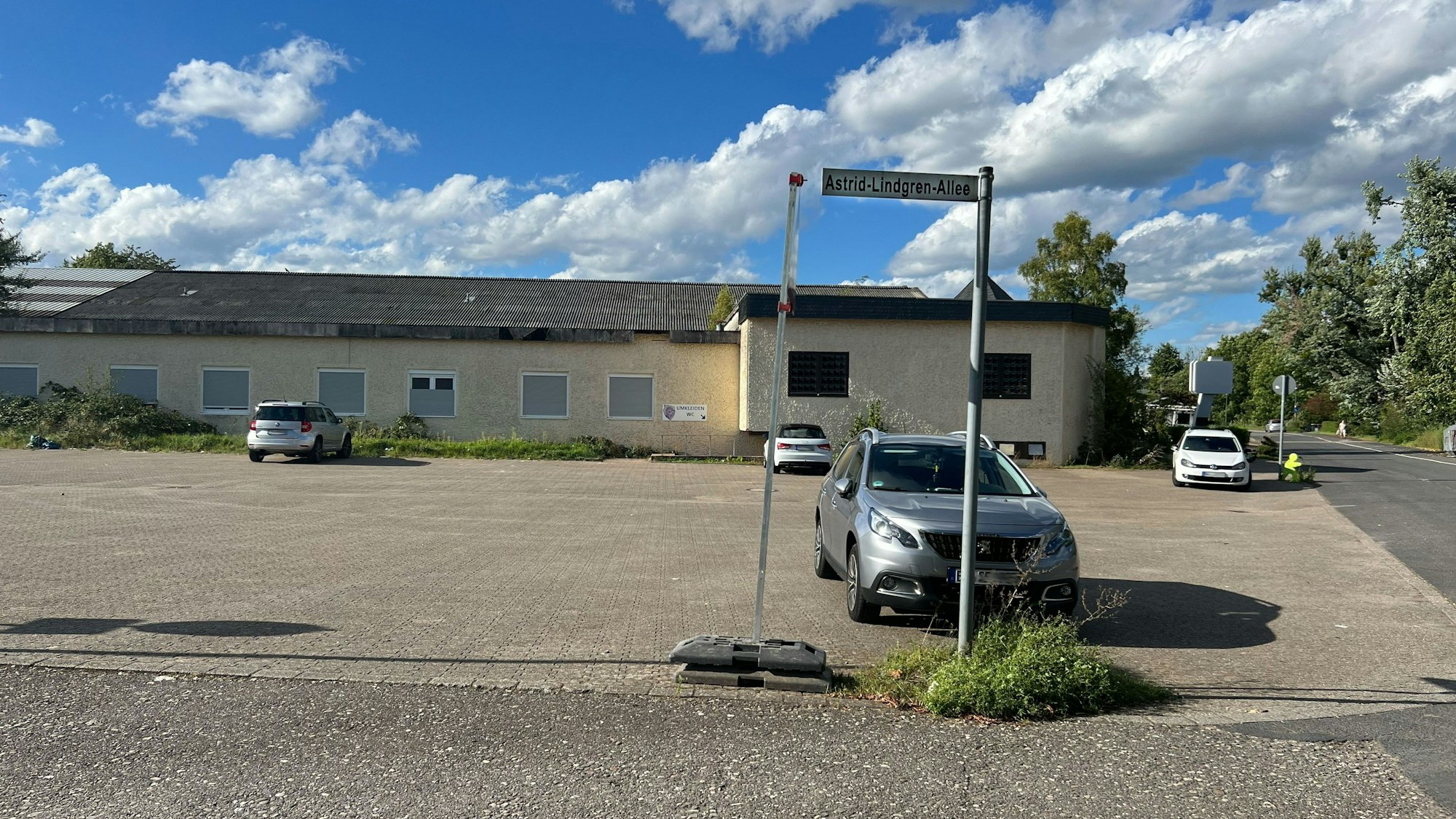 Ein fast leerer Parkplatz vor einem einstöckigen Gebäude ist zu sehen.