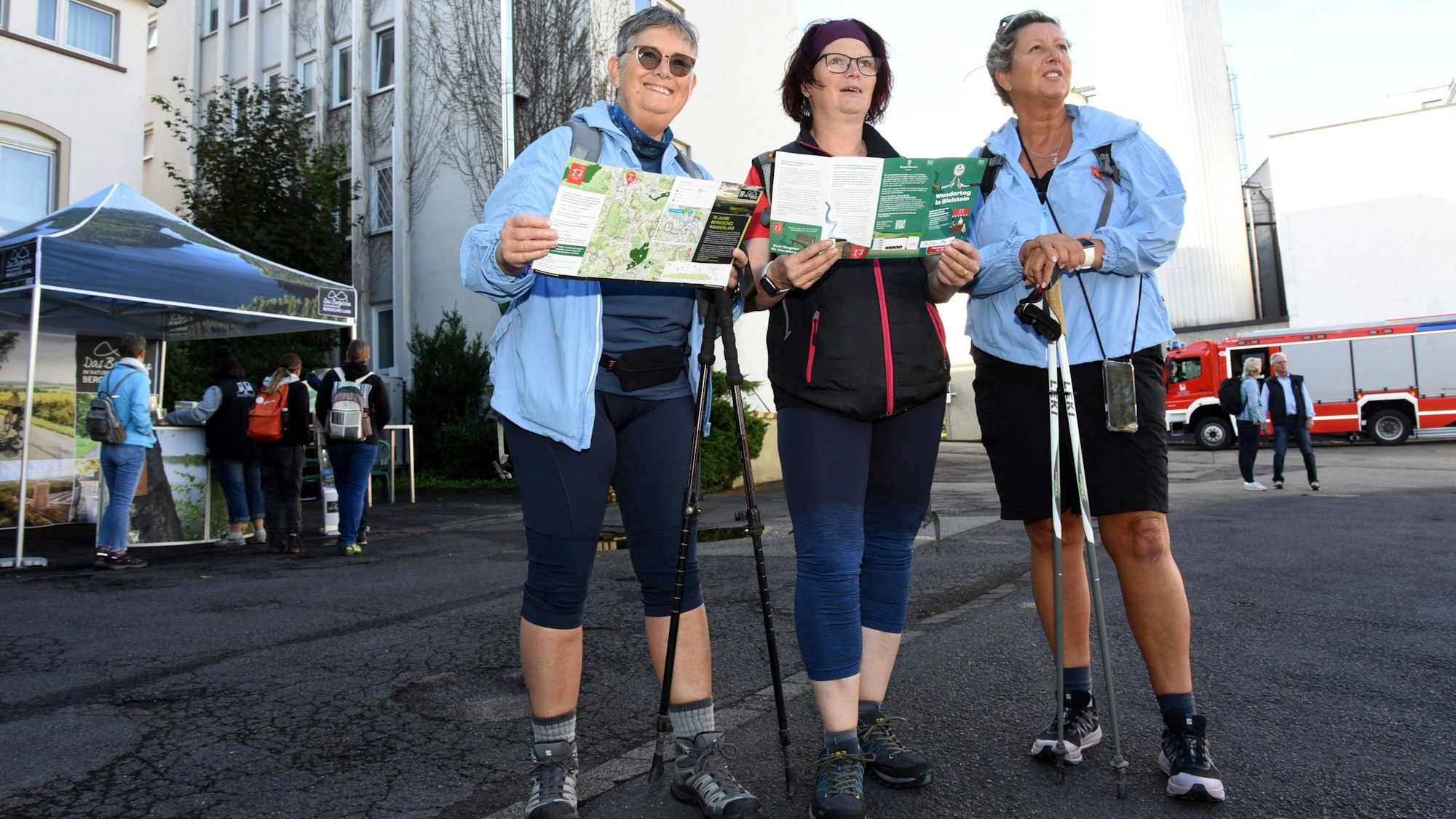 Drei Frauen in Wanderkleidung stehen nebeneinander, halten Wanderkarten in der Hand und schauen gemeinsam suchend in die Ferne.