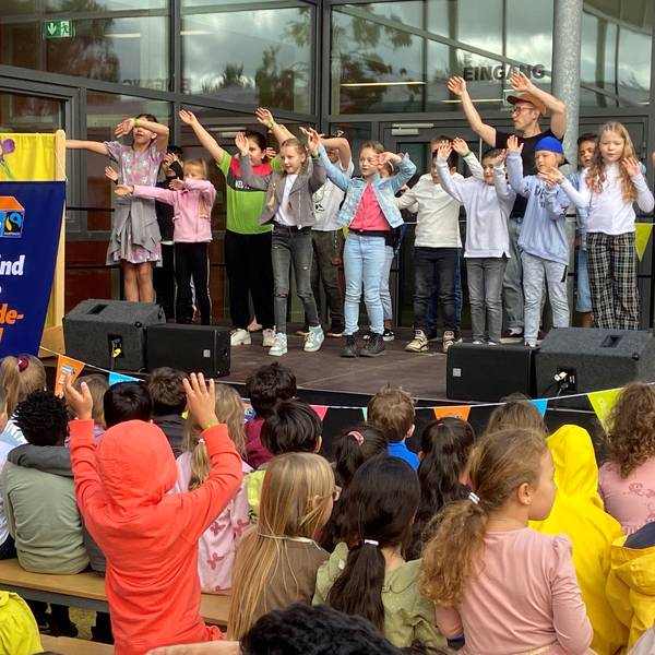 Kinder stehen mit erhobenen Armen auf einer Bühne und singen.