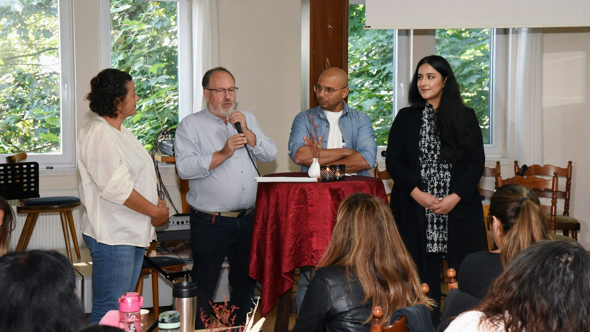 Mehrere Menschen verschiedener Kulturen stehen an einem Tisch bei einem Gespräch zusammen.