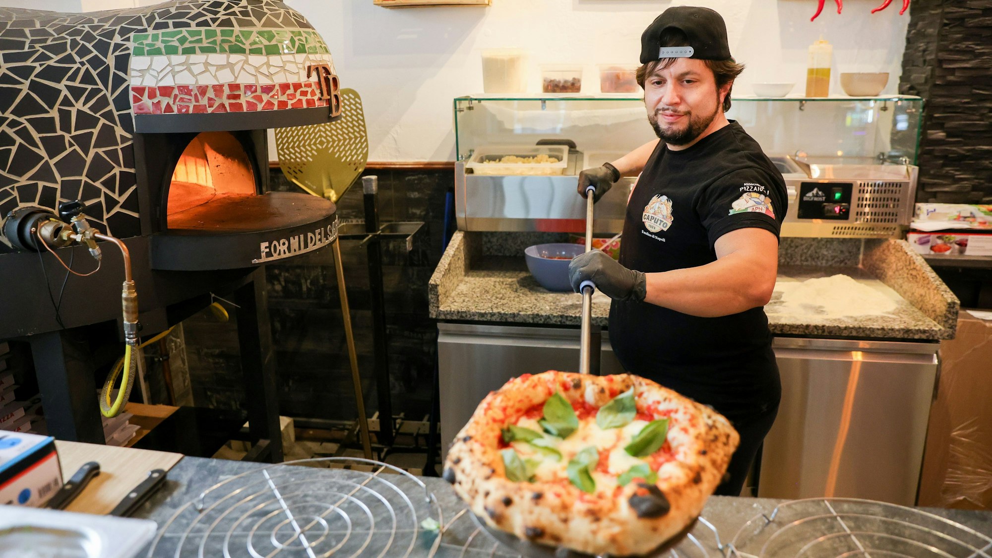 Pizzabäcker Tone präsentiert eine frisch gebackene Pizza.