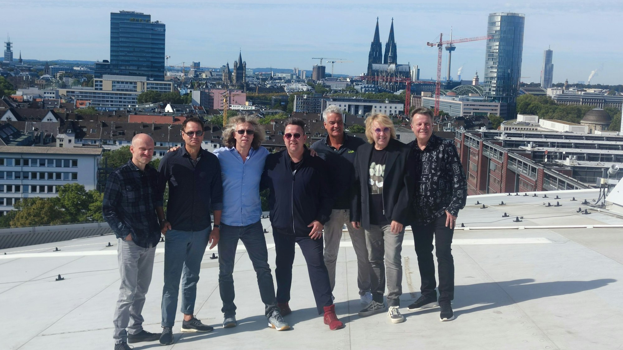 Die sieben Bandmitglieder der Band „"Die Prinzen" “stehen auf dem Dach der Lanxess Arena. Im Hintergrund sieht man das Panorama der Stadt Köln.
