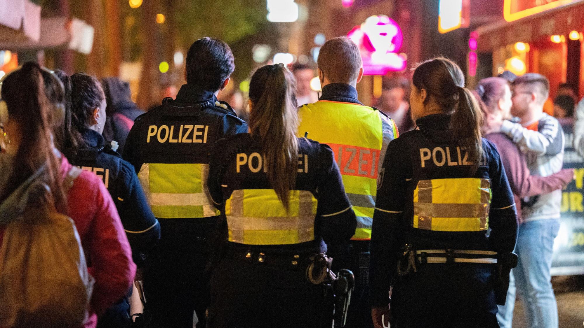 Vier Polizeibeamte gehen bei Nacht durch eine Straße voller Menschen.