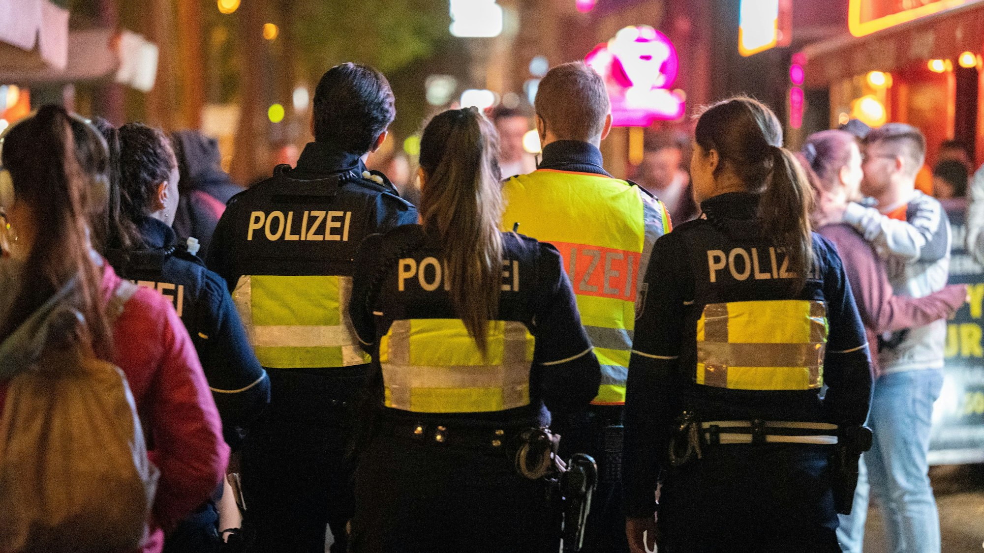 Vier Polizeibeamte gehen bei Nacht durch eine Straße voller Menschen.