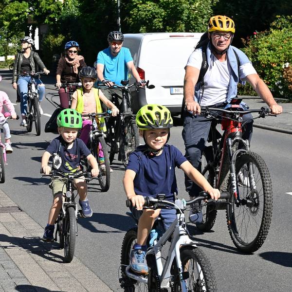Kinder auf Fahrradhelmen radeln auf der Straße neben Müttern und Vätern.