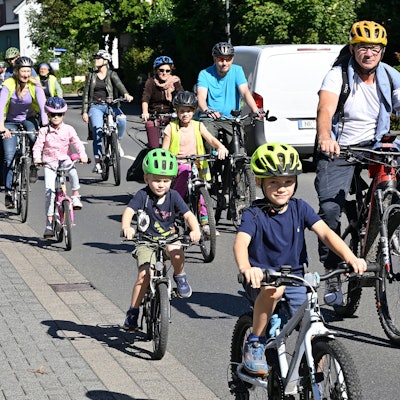 Kinder auf Fahrradhelmen radeln auf der Straße neben Müttern und Vätern.