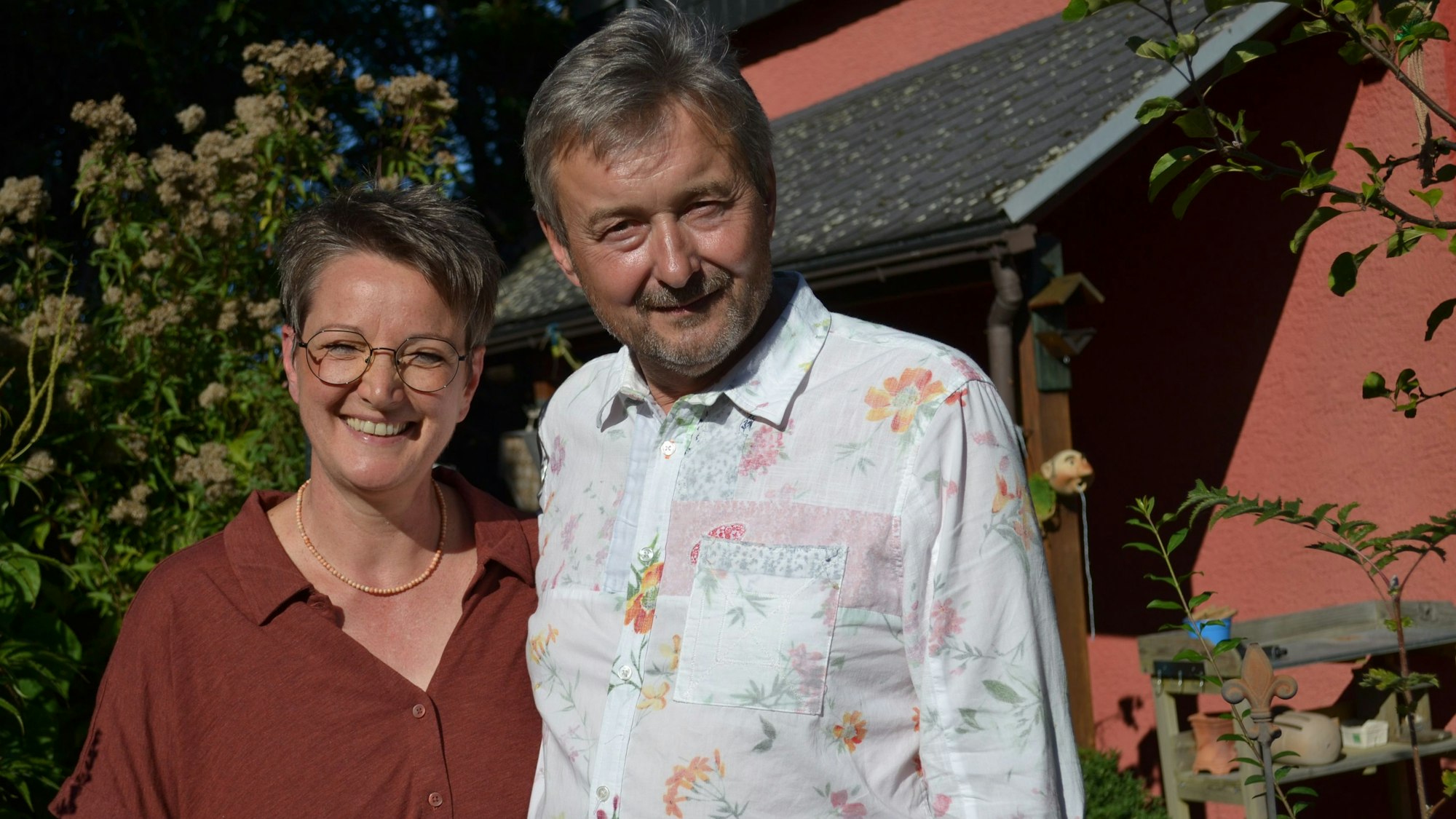 Eine Frau und ein Mann stehen Arm in Arm in ihrem Garten.