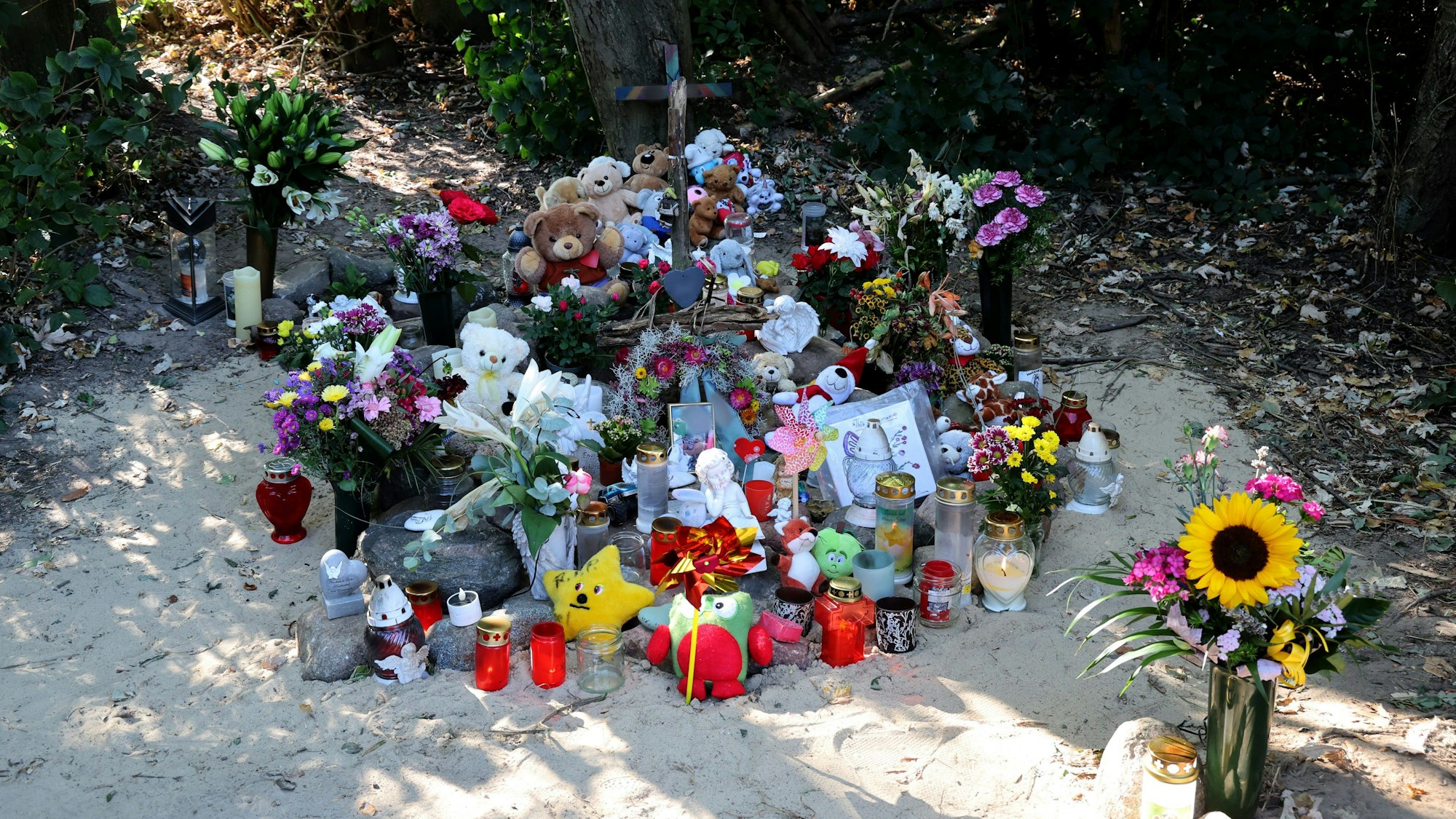An der Stelle in unmittelbarer Nähe des Sees in Pragsdorf, wo der Sechsjährige am 14.09.2023 mit schwersten Stichverletzungen gefunden wurde, an denen er später verstarb, wurden ein Kreuz, Blumen, Kerzen, Bilder und Plüschtiere aufgestellt.