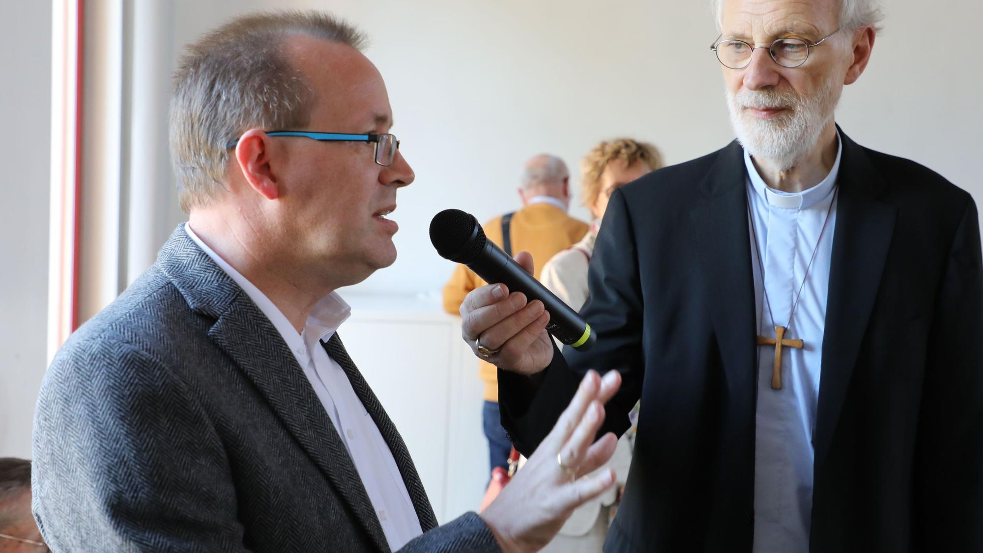 Hans Schlömer vom Pfarrgemeinderat Overath spricht in ein Mikrofon, das Weihbisch Ansgar Puff hält.