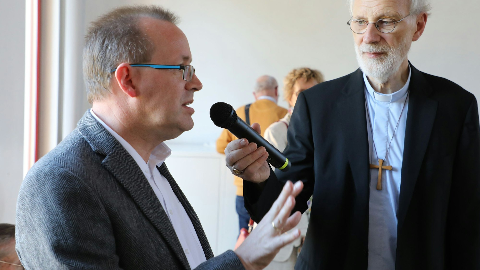 Hans Schlömer vom Pfarrgemeinderat Overath spricht in ein Mikrofon, das Weihbisch Ansgar Puff hält.