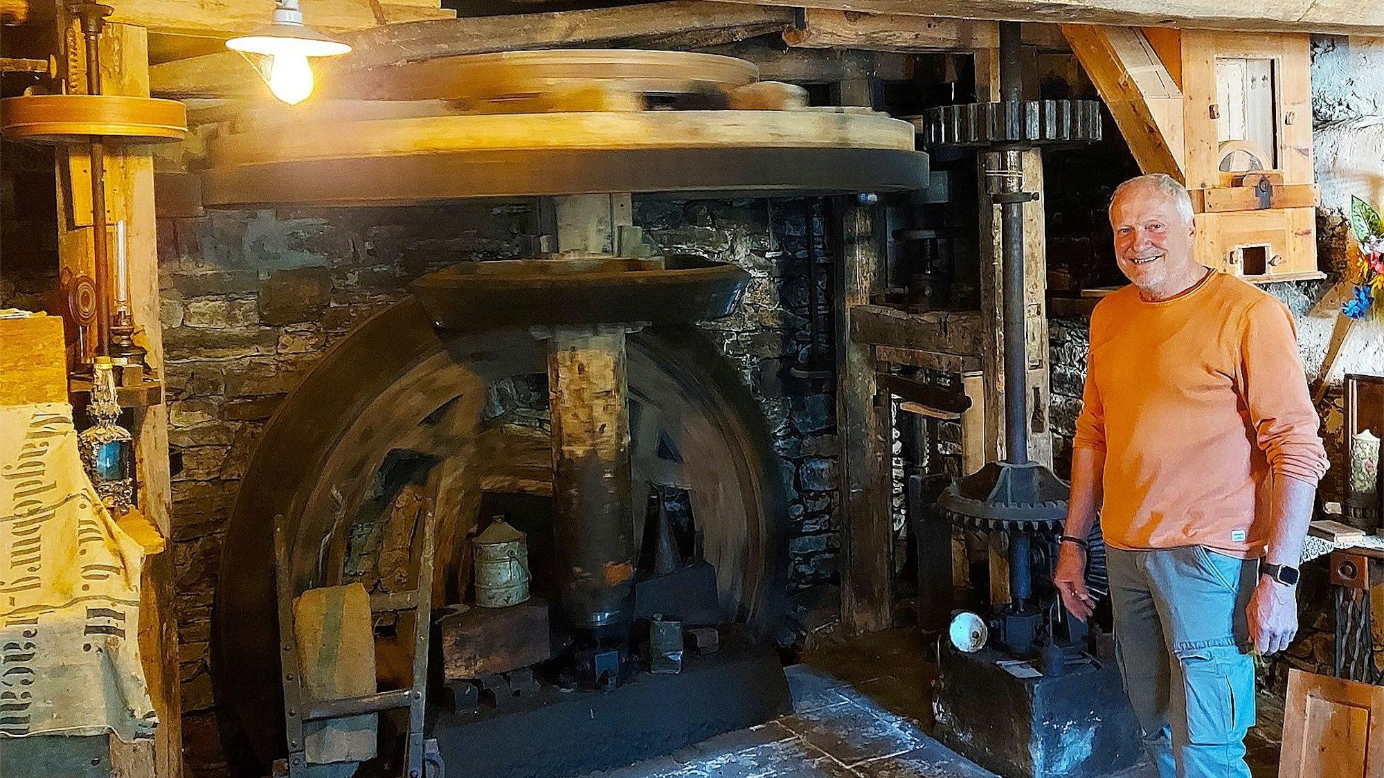 Walfried Heinen steht lächelnd in der historischen Mühle Falkenstein in Eiserfey. Eine Deckenlampe erleuchtet den Raum.