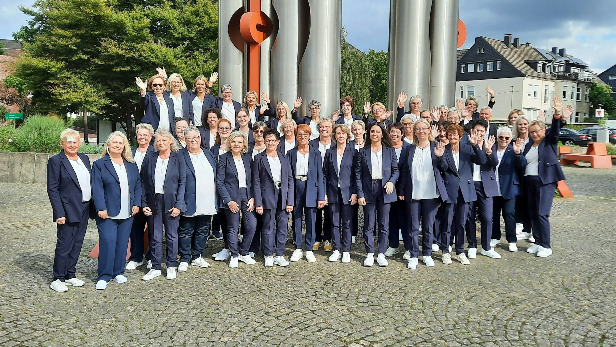 Ein Frauenchor posiert vor einer Stahlskulptur.