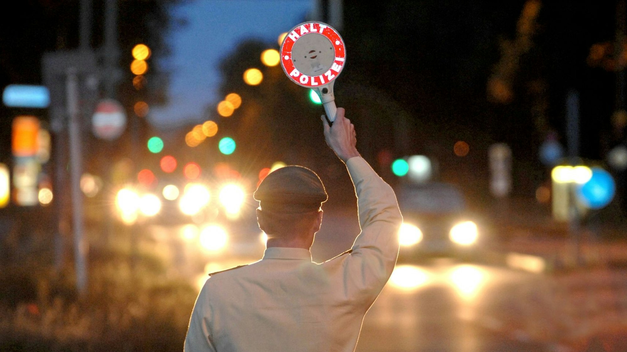 Das Bild zeigt einen Polizisten in der Dunkelheit, der Autos aus dem Verkehr winkt.
