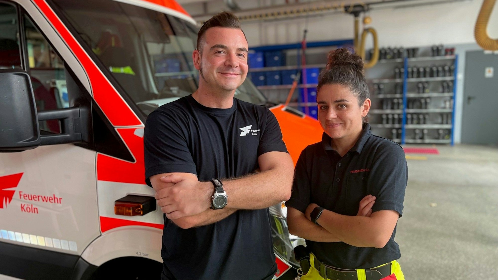 Markus Buth und Veronika Capoccia stehen in der Fahrzeughalle der Feuerwache 4 an der Äußeren Kanalstraße in Ehrenfeld vor ihrem Rettungswagen.