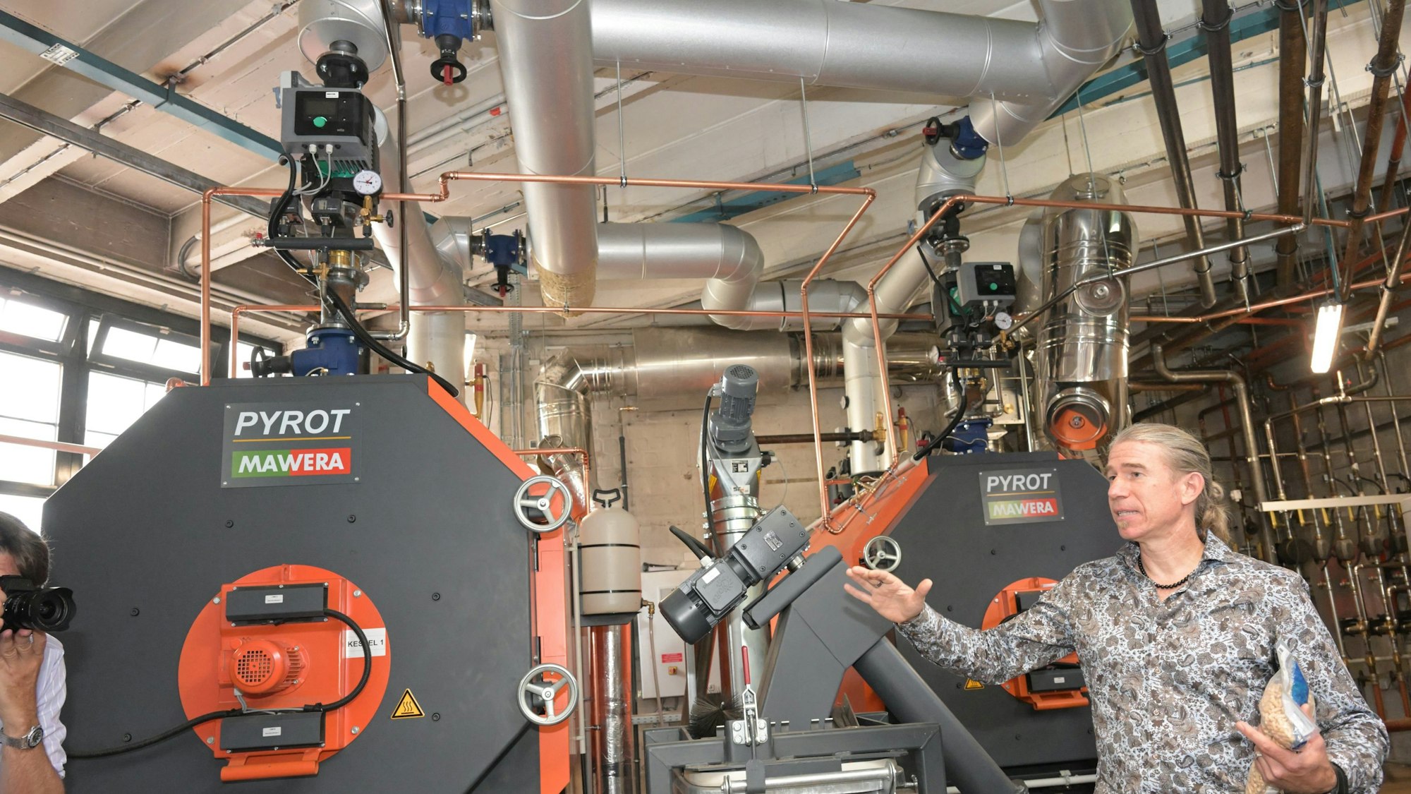 Zwei Heizungskessel sind zu sehen. Ein Mann steht daneben, um die Anlage zu erklären.