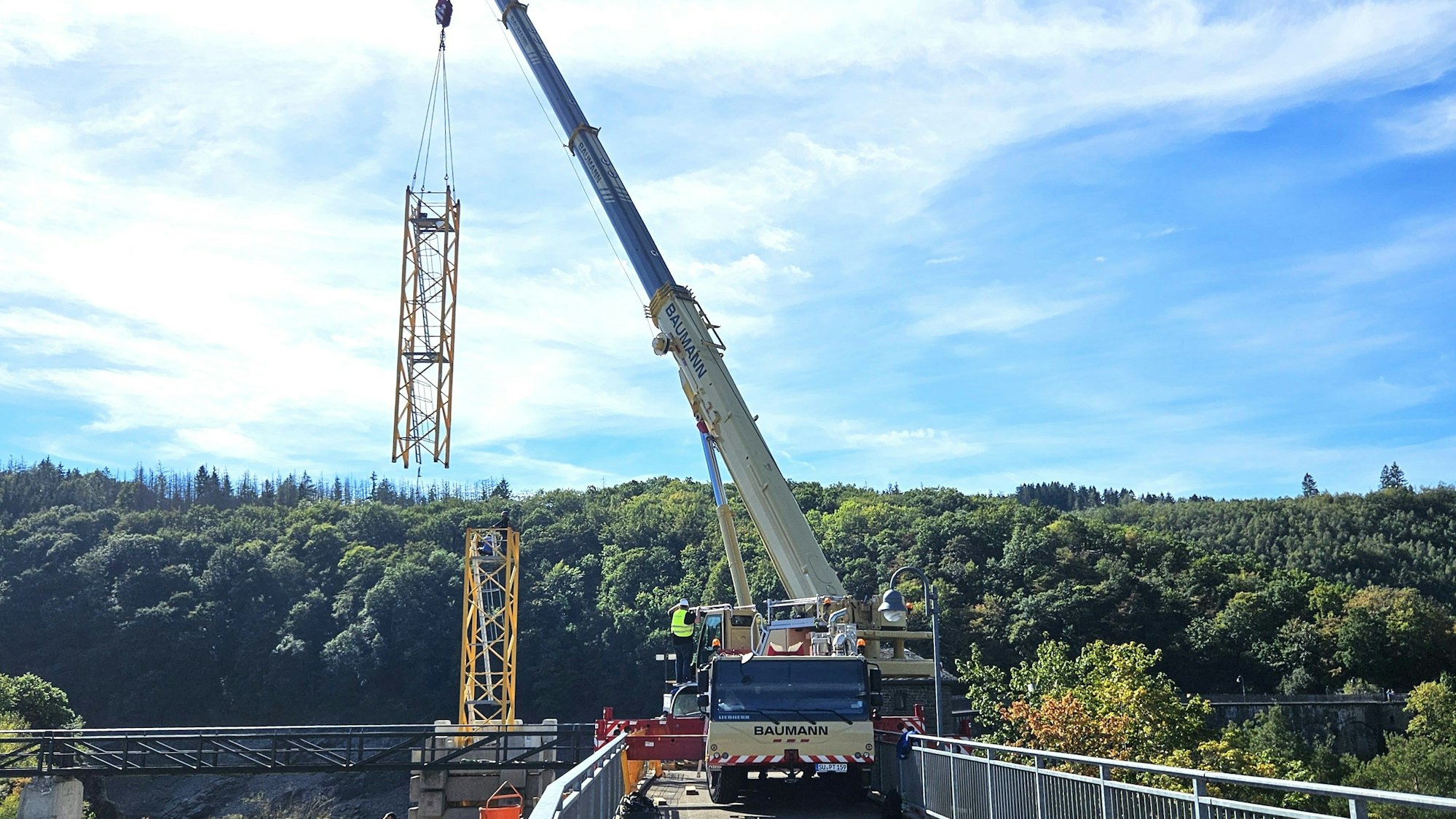 An einem Kranwagen, der auf der Urftstaumauer steht, hängen Stahleinzelteile eines Baukrans.